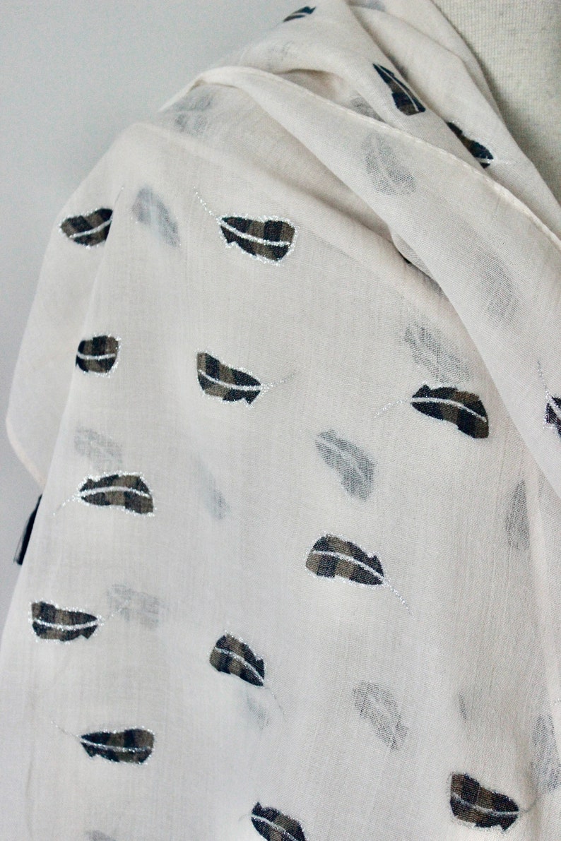 Peut inclure: Une &eacute;charpe blanche en voile avec un motif de plumes noires et brunes.