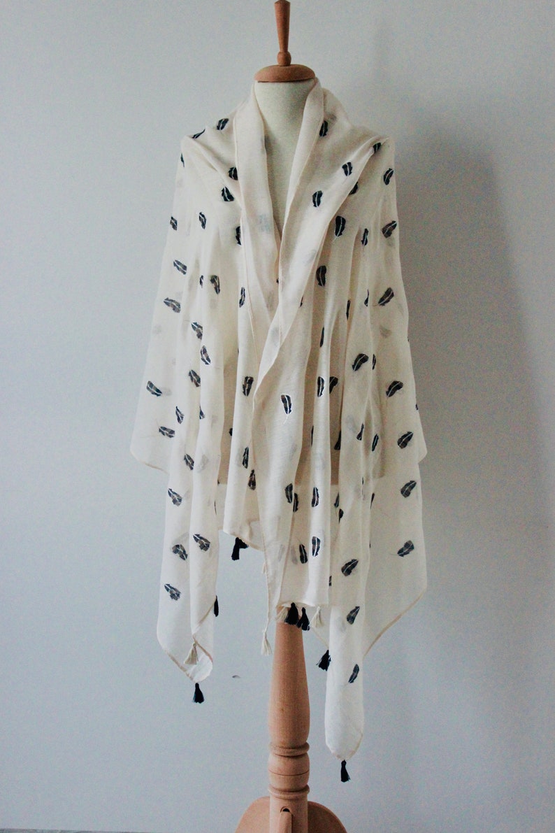 Peut inclure: Une &eacute;charpe blanche avec un motif de feuilles noires et des glands. L'&eacute;charpe est drap&eacute; sur un mannequin en bois.