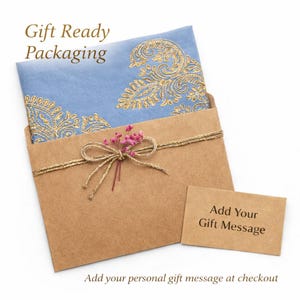 May include: Gift-ready packaging featuring a light blue card with gold floral embroidery, nestled in a brown envelope tied with gold twine and a pink floral accent. A small card reads "Add Your Gift Message."