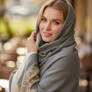 May include: A woman wearing a gray shawl with gold embroidery on the sleeves. The shawl is draped over the head and shoulders. The woman is smiling and looking at the camera.