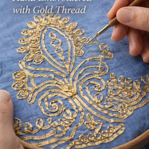 May include: Hand-embroidered design with gold thread on blue fabric, held in a wooden embroidery hoop. The text "Hand Embroidered with Gold Thread" is visible. The design features floral and scroll patterns.