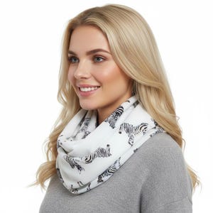 May include: White infinity scarf with a black zebra print. The scarf is wrapped around the neck of a person wearing a gray sweater. The scarf is made of a soft, lightweight material.