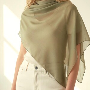 May include: A sheer, olive green scarf draped over the shoulders. The scarf has a flowing, lightweight appearance. The model is wearing a white top and cream-colored jeans. The scarf's edges are subtly outlined.