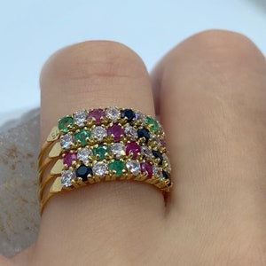 Puede incluir: Un anillo de oro con múltiples bandas engastadas con una variedad de piedras preciosas, incluyendo esmeraldas, rubíes, zafiros y diamantes.