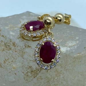 Può includere: Orecchini in oro con una pietra preziosa di rubino rosso circondata da un alone di piccole pietre bianche.