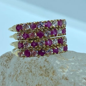 Puede incluir: Cuatro anillos apilables de oro con gemas rosas y blancas alternadas. Los anillos están colocados sobre una roca gris clara.