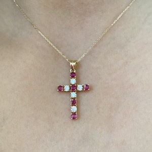 Puede incluir: Un collar de cadena de oro con un colgante de cruz de rubíes y diamantes.
