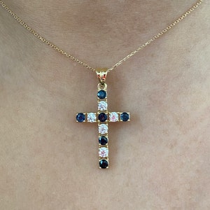 May include: A gold chain necklace with a cross pendant. The cross is adorned with alternating clear and dark blue gemstones.