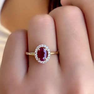 May include: A gold ring with a red oval gemstone surrounded by a halo of smaller white gemstones.