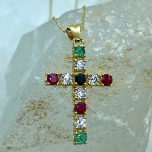May include: A gold cross pendant with a chain. The cross is adorned with small round gemstones in red, green, blue, and white.