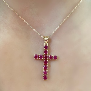 May include: A gold chain necklace with a ruby red cross pendant. The cross is made of small round rubies set in gold.