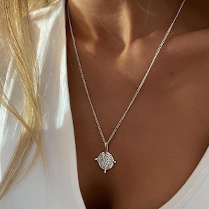 May include: A silver chain necklace with a silver pendant featuring a detailed, circular design.