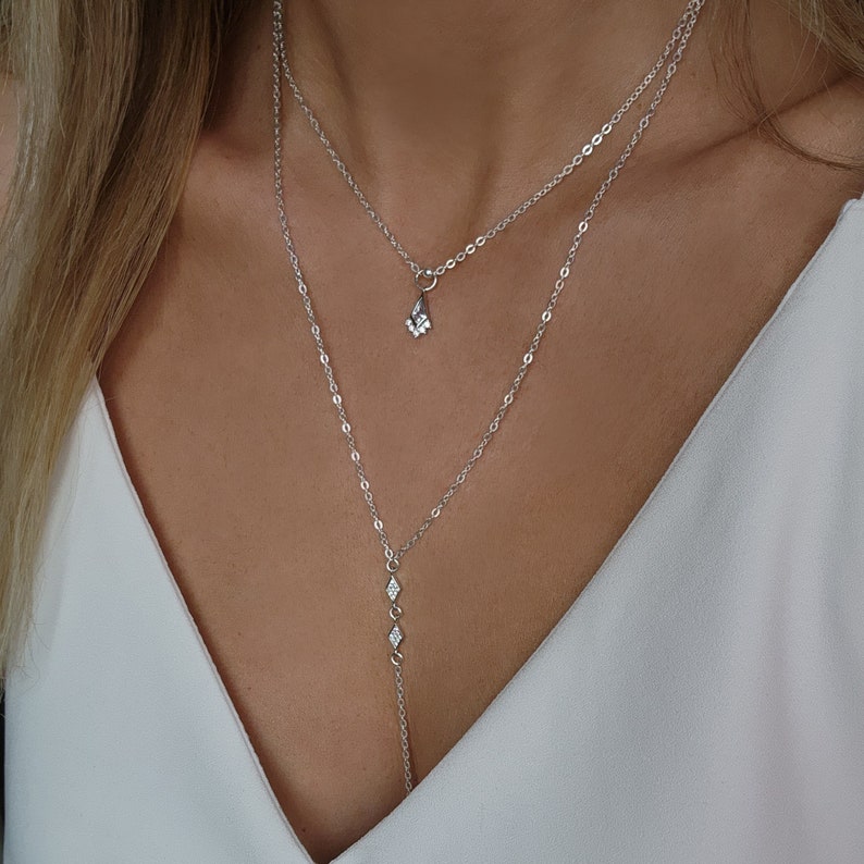 Pu&ograve; includere: Una collana argentata a due fili con un piccolo ciondolo a forma di fiore e una catena pi&ugrave; lunga con tre piccoli ciondoli a forma di diamante.