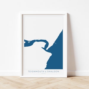 Può includere: Una stampa incorniciata bianca con una silhouette blu della costa di Teignmouth e Shaldon, Devon. Il testo "Teignmouth & Shaldon, Devon" è stampato sotto l'immagine.