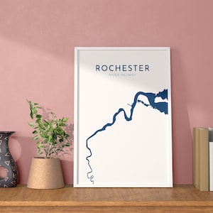 Könnte beinhalten: Ein weißer gerahmter Druck mit einer blauen Umrandung des Rochester River Medway. Der Druck befindet sich auf einem Holzregal mit einer Vase und einer Topfpflanze.