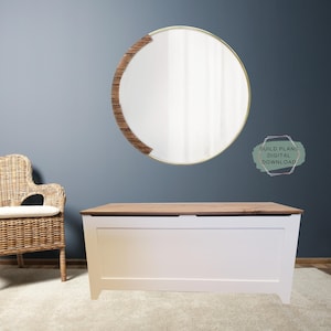 May include: White toy chest with a wood top lid. The chest is sitting on a light beige rug in front of a blue wall. A round mirror with a wood frame is hanging on the wall. The text "BUILD PLANS DIGITAL DOWNLOAD" is written in a green circle on the wall.
