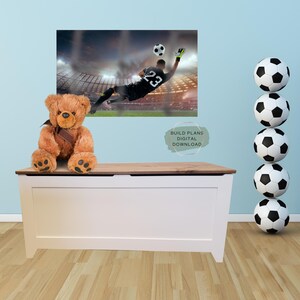 May include: A white toy chest with a wooden top. A brown teddy bear sits on the top of the chest. A soccer ball is in the background. The text "BUILD PLANS DIGITAL DOWNLOAD" is on the wall.
