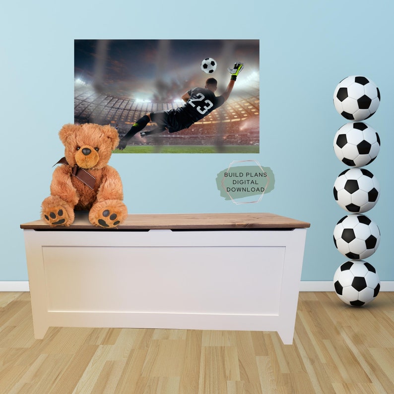 May include: A white toy chest with a wooden top. A brown teddy bear sits on the top of the chest. A soccer ball is in the background. The text "BUILD PLANS DIGITAL DOWNLOAD" is on the wall.