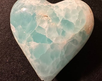 May include: A heart-shaped piece of blue and white celestite crystal. The crystal has a smooth, polished surface and a natural, organic shape.