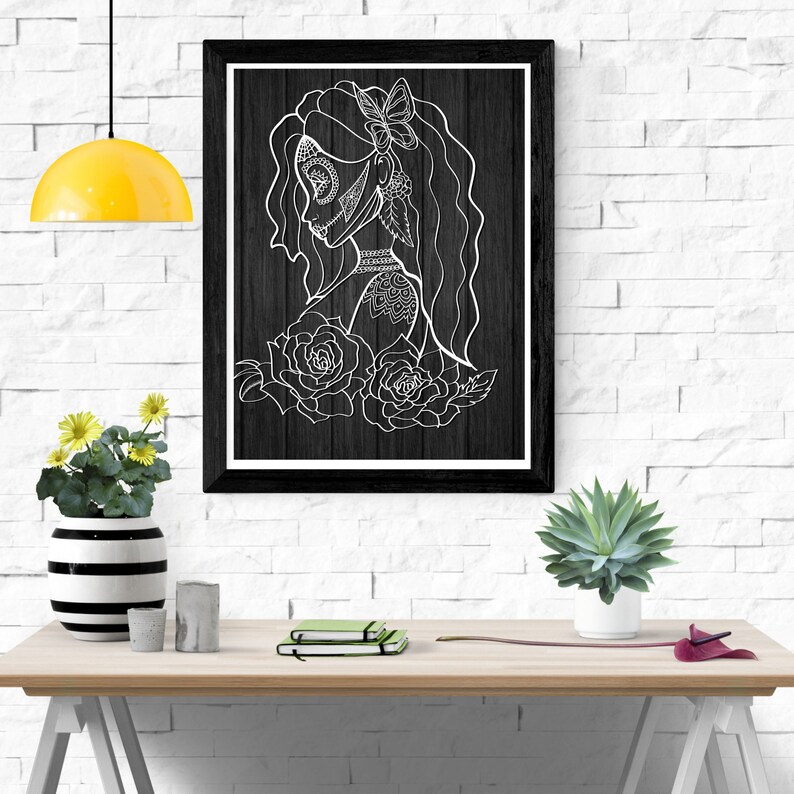 K&ouml;nnte beinhalten: Schwarz-wei&szlig;-Linienkunst-Druck einer Frau mit floralem Design. Die Frau hat ein Zucker Sch&auml;del Gesicht und einen Schmetterling im Haar. Der Druck ist in einem schwarzen Rahmen gerahmt und h&auml;ngt an einer wei&szlig;en Backsteinwand.