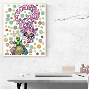 May include: A framed art print featuring a whimsical illustration of the Cheshire Cat from Alice in Wonderland. The cat is pink with a large grin, and a green caterpillar is smoking a pipe. The background is white with colorful polka dots.