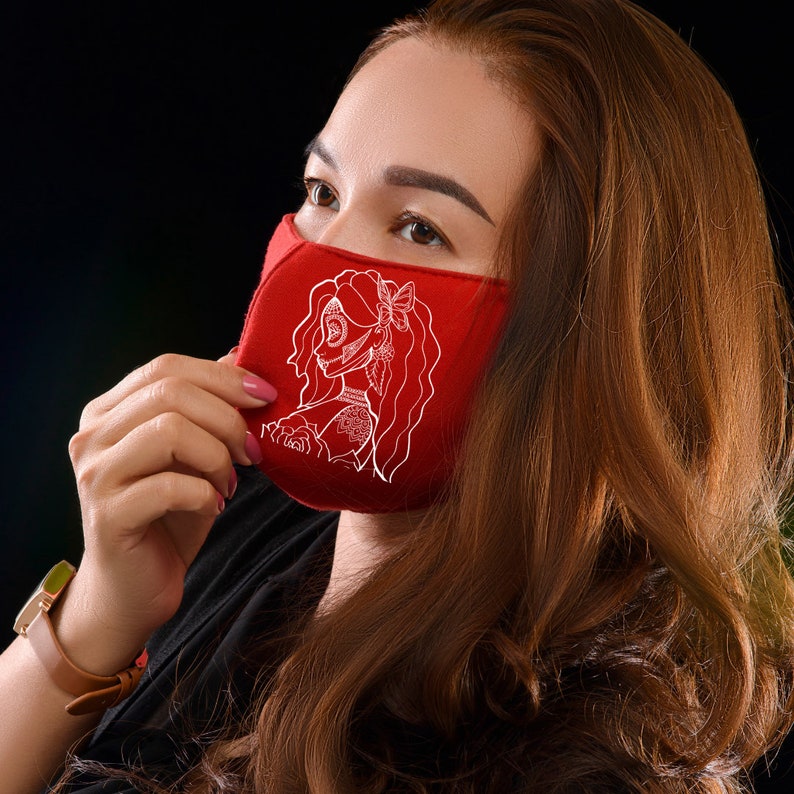 K&ouml;nnte beinhalten: Eine rote Gesichtsmaske mit einem wei&szlig;en Design einer Frau mit einer Blume im Haar. Die Maske ist aus Stoff und hat einen wei&szlig;en Rand.
