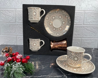 May include: A set of three Turkish coffee cups and saucers with a gold geometric pattern on a white background. The cups and saucers are in a black box with a copper coffee pot.