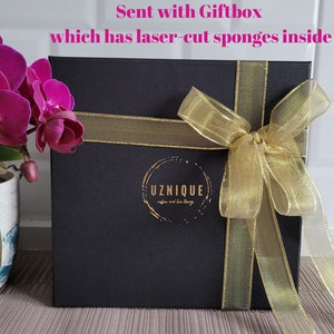 May include: A black gift box with a gold ribbon and bow. The box has a gold logo that says "UZNIQUE coffee and tea shop". The text "Sent with Giftbox which has laser-cut sponges inside" is written in pink above the box.