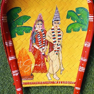 May include: A hand-painted wooden tray with a yellow background and red border. The tray features a painted scene of a bride and groom in traditional Indian wedding attire. The bride is wearing a red sari and the groom is wearing a white dhoti. The tray is decorated with green palm trees and a red canopy.