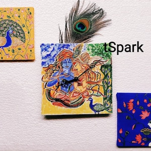May include: Three square wall art pieces with a blue peacock, a colorful painting of a couple with a peacock feather, and a blue floral design with a white cow. The middle piece is a clock with the text "tSpark".