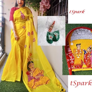 May include: A yellow saree with intricate embroidery and a woman wearing it. The saree has a green and red design with a woman in a yellow dress embroidered on the bottom. The saree is paired with a red blouse. The image also includes a hand-painted wooden tray with a scene of a wedding ceremony.