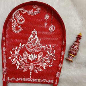 May include: A red woven tray with white painted designs, featuring a woman figure and a lotus flower. A small wooden bottle stopper with red, yellow, and gold accents is placed next to the tray.
