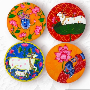 May include: Four round decorative plates with colourful painted designs. Each plate features a different scene with a cow, a lotus flower, a deity, and a hand with a lotus flower. The plates are perfect for adding a touch of Indian art to your home decor.