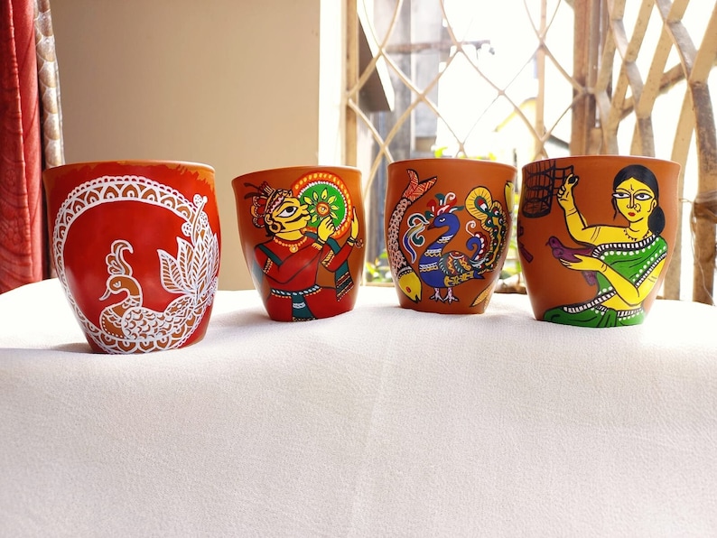 Op de afbeelding: Vier terracotta bekers met handgeschilderde ontwerpen. De bekers tonen een pauw, een man die een muziekinstrument bespeelt, een pauw met een vis en een vrouw die een vogel vasthoudt.