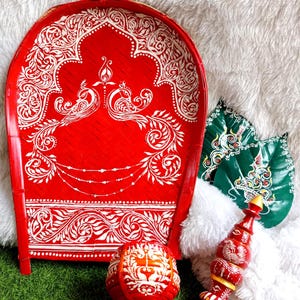 May include: A red decorative tray with white ornate designs and two peacocks. The image also features a red and white decorative ball, a red and gold decorative item, and two green leaf-shaped decorations.