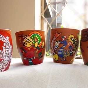 Op de afbeelding: Vier terracotta bekers met handgeschilderde ontwerpen. De bekers tonen een pauw, een muzikant, een pauw met een vis en een vrouw die een vogelkooi vasthoudt.