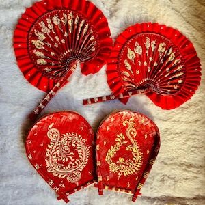May include: Four red hand fans with gold decorative patterns. Two fans are round and pleated, with a handle. The other two are a heart shape with a woven texture and a handle. All fans have gold floral designs.