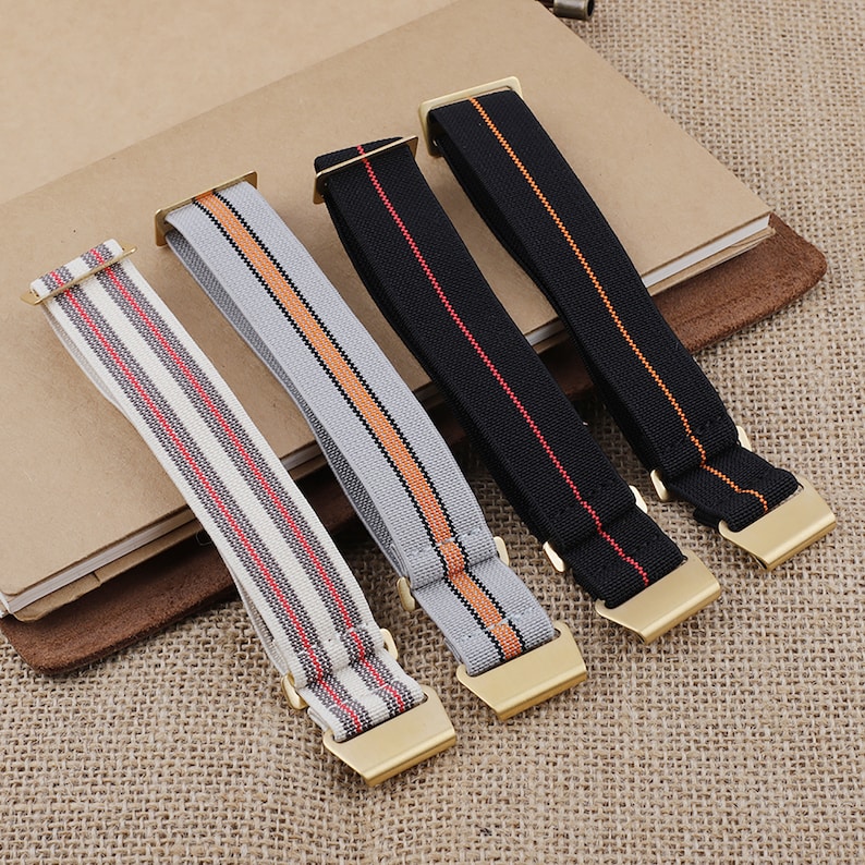 Puede incluir: Cuatro correas de reloj diferentes con hebillas doradas. Las correas est&aacute;n hechas de material el&aacute;stico con patrones rayados en negro, rojo, naranja y gris.
