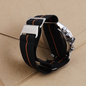 Puede incluir: Una correa de reloj negra con costuras naranjas y una hebilla plateada. La correa est&aacute; hecha de nylon y est&aacute; dise&ntilde;ada para un reloj con una anchura de leng&uuml;eta de 20 mm.