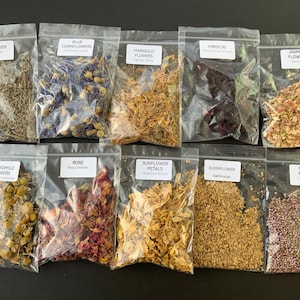 May include: An overhead shot of ten clear plastic bags filled with dried flowers. The bags are labeled with the names of the flowers: lavender, blue cornflowers, marigold, hibiscus, jasmine, chamomile, rose, sunflower petals, elderflower, and heather.