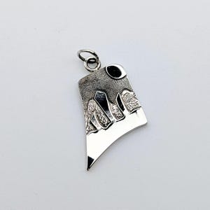 May include: A silver pendant featuring an abstract landscape design with a textured, dark gray upper section and a smooth, polished silver lower section. The piece includes a small circular bail at the top and depicts stylized mountain peaks.