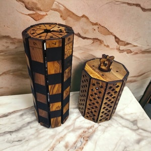 May include: Two wooden boxes with intricate designs. The larger box is a cylinder with a checkered pattern and numbers 6 and 7 visible. The smaller box has a diamond pattern and a crown-shaped top.