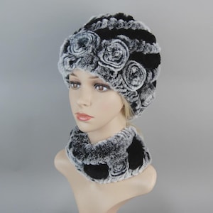May include: A black and white faux fur hat and neck warmer set. The hat features three floral designs. The neck warmer has a matching floral pattern. The set is designed to keep the wearer warm and stylish.