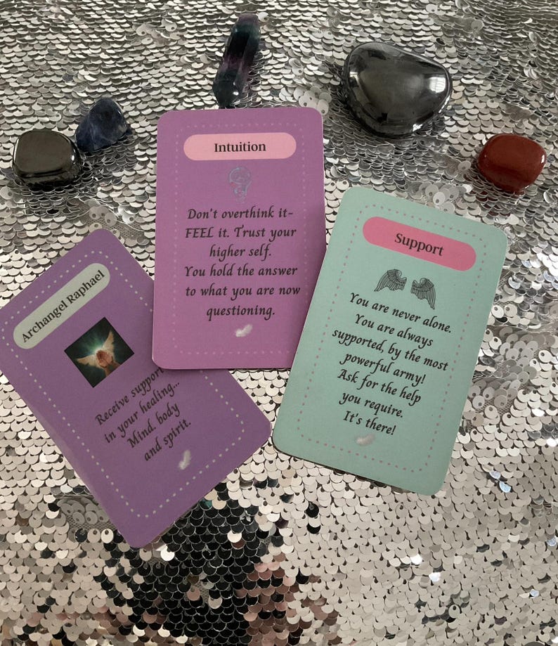 May include: Three purple, green, and blue oracle cards with angel wings and inspirational messages. The cards read "Archangel Raphael", "Intuition", and "Support".