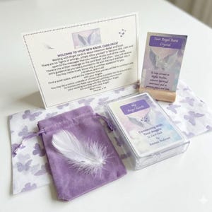 May include: An angel card deck set with a purple velvet pouch, a white feather, and a card holder. The deck is in a clear plastic case, with the title "Connecting With Your Angels." The set includes a card with the text "Your Angel Aura Crystal."