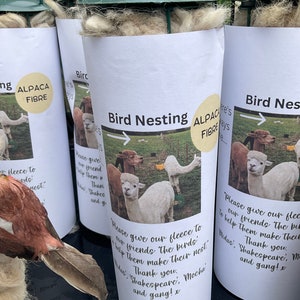 May include: Three white bird nesting boxes made of alpaca fiber. The boxes are labeled "Bird Nesting" and feature a photo of alpacas with the text "Please give our fleece to our friends the birds. Help them make their nest. Thank you. Shakespeare, Mocha and gang! x"