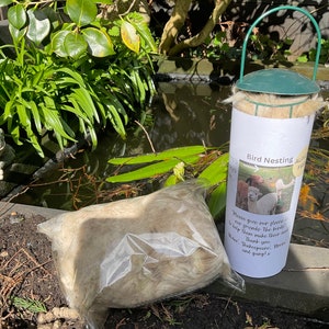 May include: A white bag filled with fluffy alpaca fleece sits next to a green and white bird nesting box. The box has a label that reads "Bird Nesting Alpaca Fleece" and includes instructions to give the fleece to birds to help them make their nests. The label also includes a thank you message from "Shakespeare, Morde and gang!"