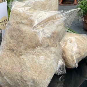 May include: Two clear plastic bags filled with light brown alpaca fiber. The bags are labeled "Alpaca Fibre".