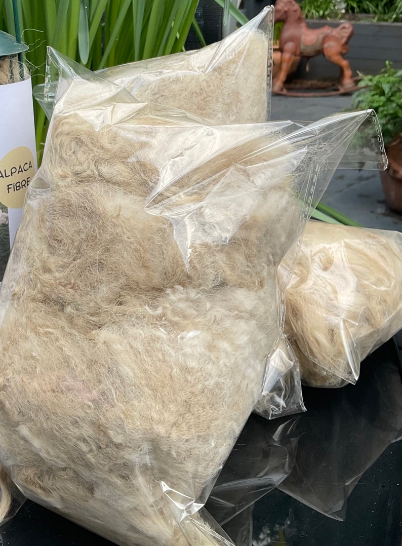 May include: Two clear plastic bags filled with light brown alpaca fiber. The bags are labeled "Alpaca Fibre".
