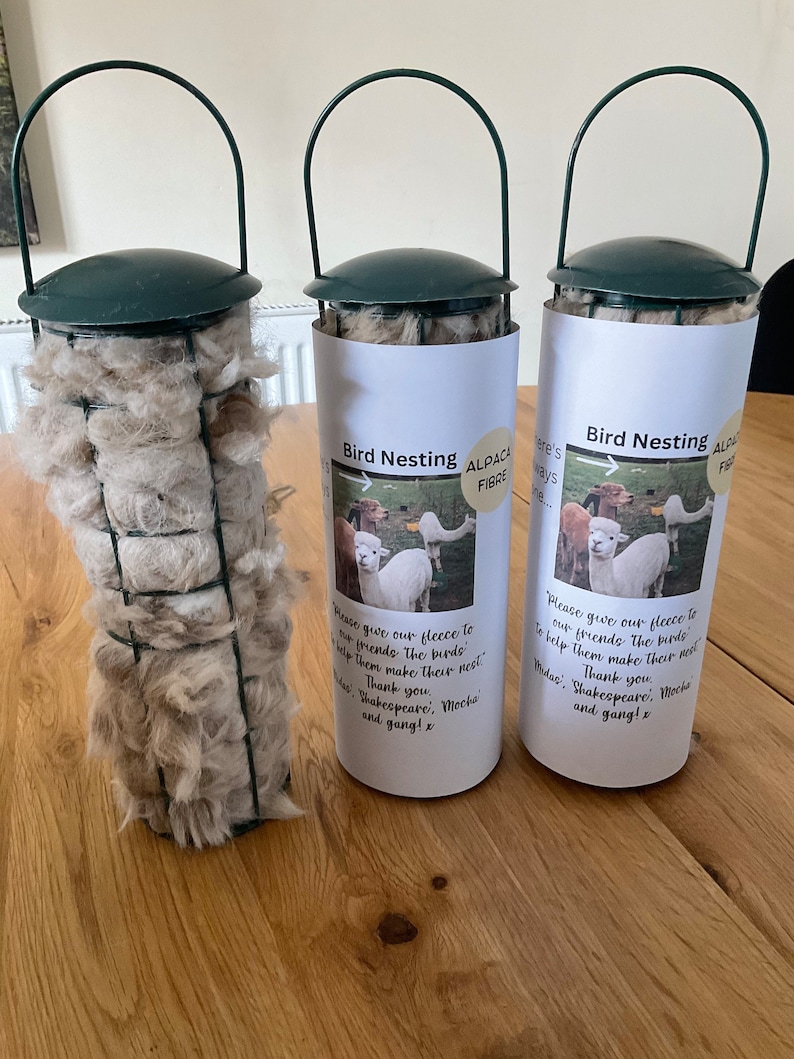 May include: Three green bird feeders filled with alpaca fleece. The feeders have a white label with the text "Bird Nesting Alpaca Fibre" and a message from the alpaca farm owners thanking customers for helping birds make their nests.